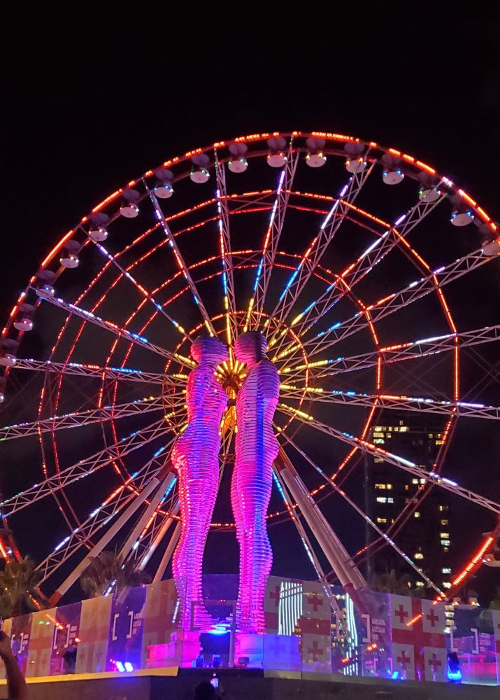 Statue d'Ali et Nino sur le point de s'embrasser de nuit  toute illuminée de rose, avec la grand roue de Batoumi en arrière plan