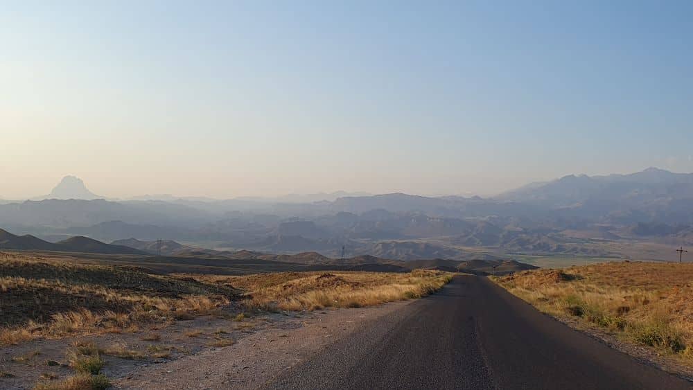 une route qui plonge vers la vallée avec les montagnes au loin à la lumière du soir